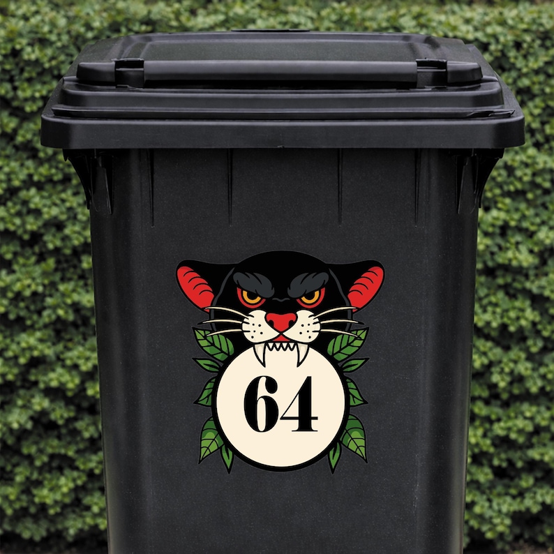 May include: Black trash bin with a decorative sticker featuring a black panther head with red ears and a red nose. The panther is above a white circle with the number 64. Green leaves surround the circle.