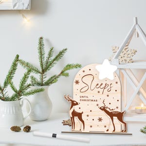 May include: A wooden countdown calendar with a white star on top. The calendar features two deer with the text "Sleeps Until Christmas".