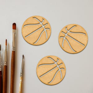Puede incluir: Tres adornos de madera con forma de bal&oacute;n de baloncesto con un acabado de madera marr&oacute;n. Los adornos est&aacute;n recortados en forma de bal&oacute;n de baloncesto con un contorno negro.