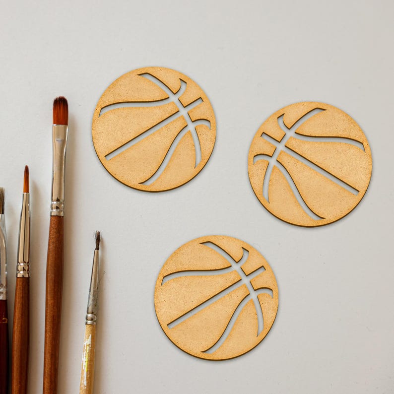 Puede incluir: Tres adornos de madera con forma de bal&oacute;n de baloncesto con un acabado de madera marr&oacute;n. Los adornos est&aacute;n recortados en forma de bal&oacute;n de baloncesto con un contorno negro.