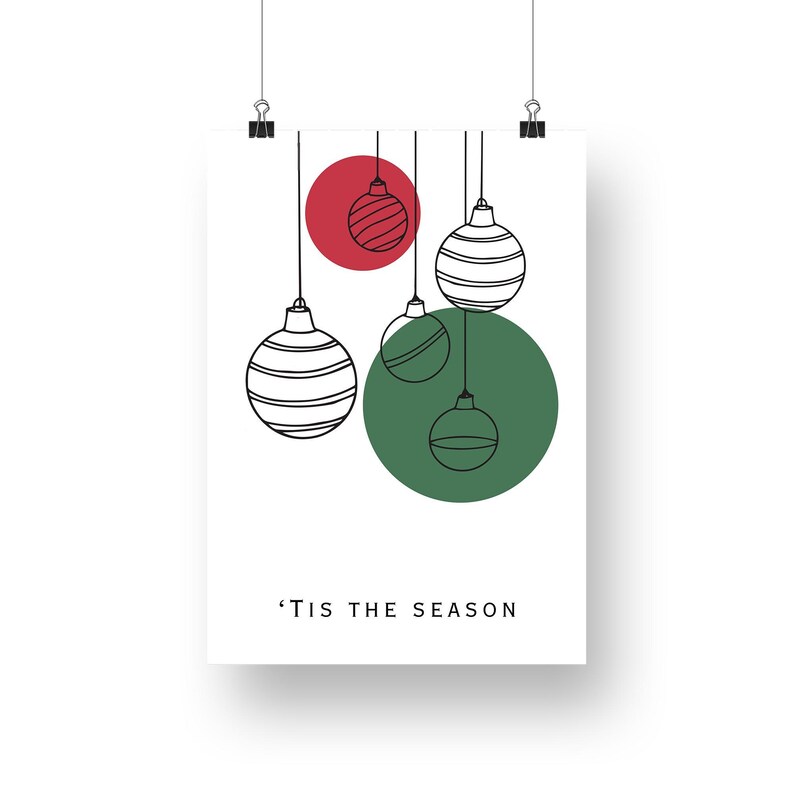 K&ouml;nnte beinhalten: Ein wei&szlig;er druckbarer Kunstdruck mit einem gr&uuml;nen Kreis und einem roten Kreis mit schwarzen umrandeten Weihnachtskugeln, die von oben h&auml;ngen. Der Text 'Tis the Season befindet sich am unteren Rand des Drucks.