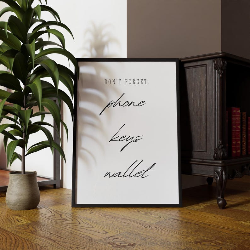 May include: A black framed print with white background and black text that reads "Don't forget: phone, keys, wallet".