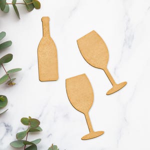 Puede incluir: Dos copas de vino de madera y una botella de vino de madera recortada. Las copas y la botella son de color marr&oacute;n claro y tienen una textura rugosa.