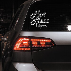 May include: A silver car with a white vinyl sticker on the rear window that reads "Hot Mess Express".