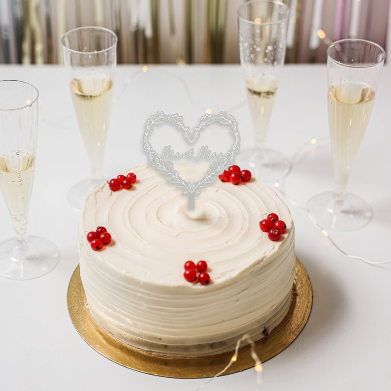 May include: A white wedding cake with red berries and a silver heart-shaped topper that says "Mr. & Mrs."