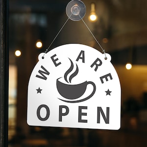 May include: White, arched sign with the words "WE ARE OPEN" in black, featuring a coffee cup graphic. The sign is suspended by a string and suction cup, indicating a business is open. Stars flank the coffee cup.