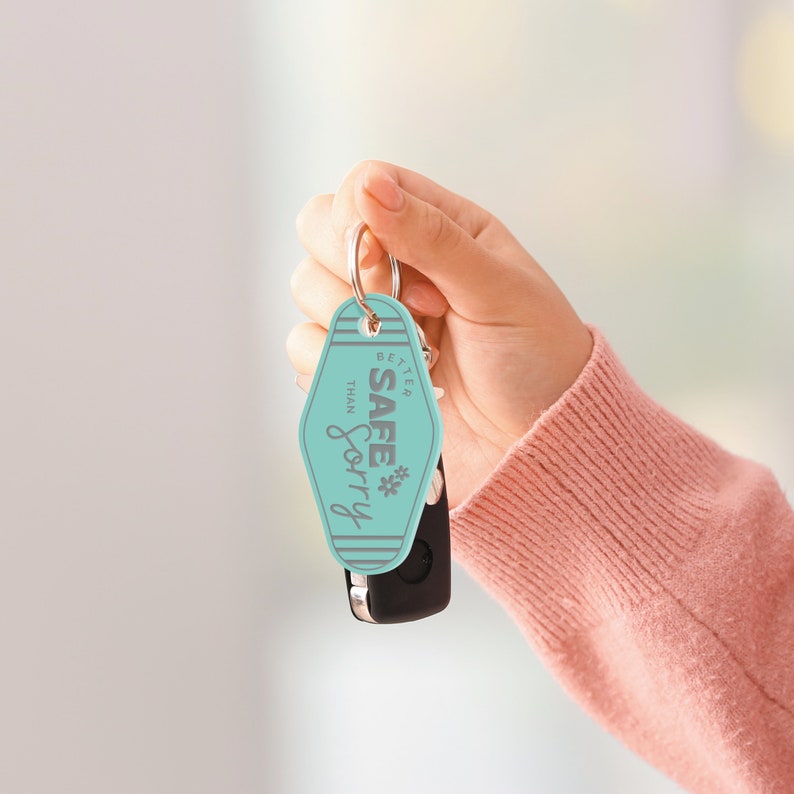 May include: A turquoise blue keychain with the text "Better Safe Than Sorry" in gray lettering. The keychain is in the shape of a motel key tag.