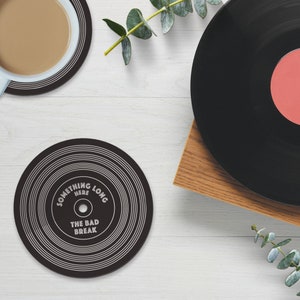Puede incluir: Posavasos de vinilo negro y blanco con el texto "Something Here Long The Bad Break".