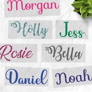 May include: A selection of name decals in different colours and fonts. Names include "Morgan," "Holly," "Jess," "Rosie," "Bella," "Daniel," and "Noah." The decals are presented on a white background.