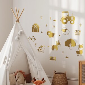 Op de afbeelding: Gouden wanddecoraties met boerderijdieren, waaronder een tractor, een schuur, een varken, een koe, een paard, een schaap, een lama en een boom. De stickers bevinden zich op een witte muur met een witte tipi-tent op de voorgrond.
