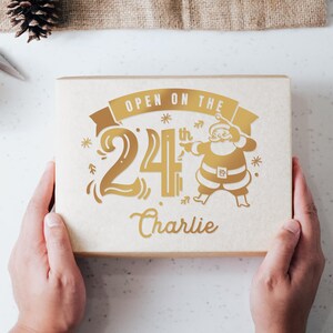 May include: A gold gift box with the text "Open on the 24th Charlie" and a cartoon image of Santa Claus.