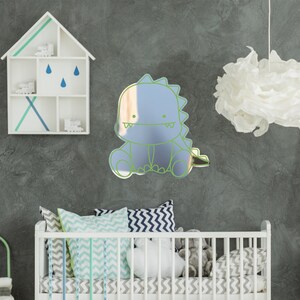 May include: A light blue dinosaur-shaped mirror with a green outline, hanging on a gray wall above a white crib with blue and green patterned bedding.