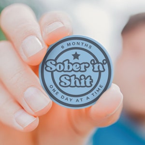Puede incluir: Una ficha redonda azul con el texto "6 Months Sober 'n' Shit One Day At A Time" en letras negras.