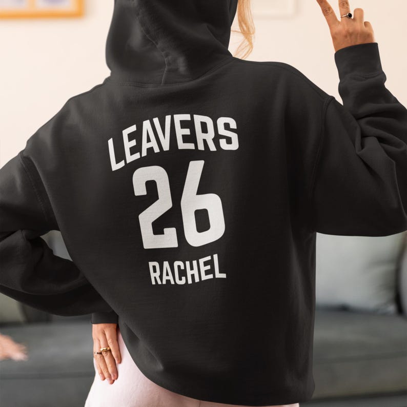 May include: Black hoodie with the word "LEAVERS" above the number "26" and the name "RACHEL" in white block letters. The hoodie has a hood and is made of a soft material.