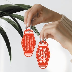 May include: Two red keychains with white text. One keychain says "SEVERE NUT ALLERGY EpiPen in bag! In case of emergency, please contact my mother, Shelly, at 01234 123456." The other keychain says "Medical + Info!+".