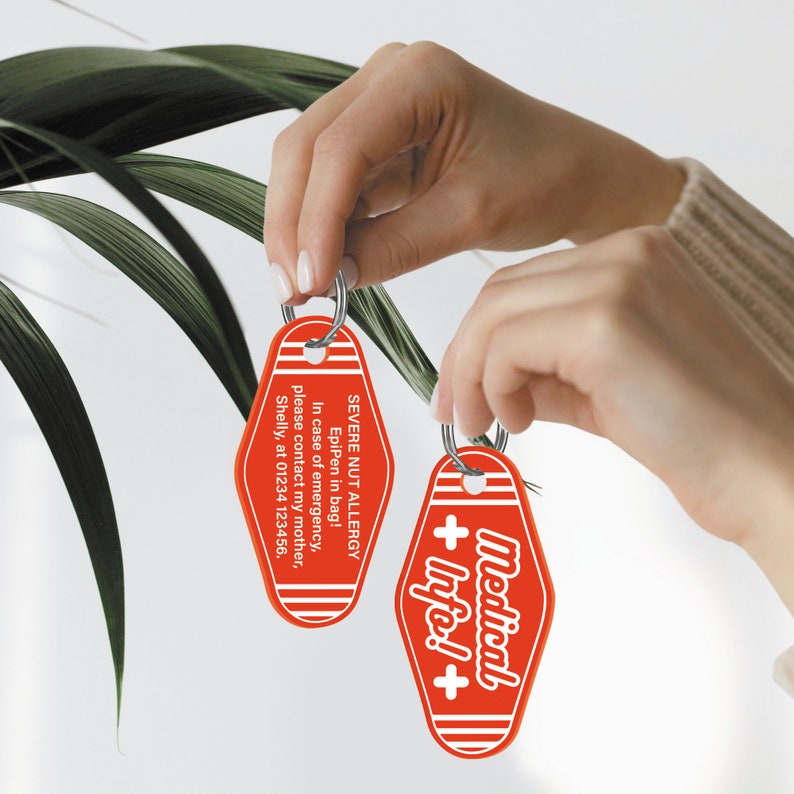 May include: Two red keychains with white text. One keychain says "SEVERE NUT ALLERGY EpiPen in bag! In case of emergency, please contact my mother, Shelly, at 01234 123456." The other keychain says "Medical + Info!+".