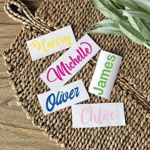 May include: Five personalized name stickers with different names written in colorful cursive lettering. The names are Harry, Michelle, James, Oliver, and Chloe.