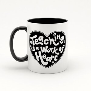 Puede incluir: Taza de cer&aacute;mica blanca con interior y asa negros. La taza presenta un coraz&oacute;n negro con el texto "Teaching is a work of heart" en letras blancas.