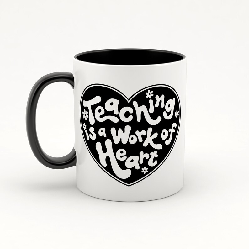 Puede incluir: Taza de cer&aacute;mica blanca con interior y asa negros. La taza presenta un coraz&oacute;n negro con el texto "Teaching is a work of heart" en letras blancas.