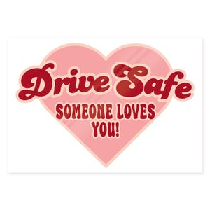 May include: A pink heart-shaped sticker with the words "Drive Safe" in red, retro-style lettering. Below, the text "SOMEONE LOVES YOU!" is also in red. The sticker is designed to be placed on a car or other vehicle.