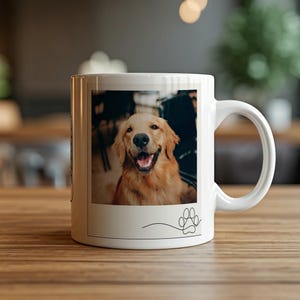 May include: White ceramic mug featuring a smiling golden retriever dog. The image is framed with a thin black line and a paw print graphic. The mug is on a wooden surface.