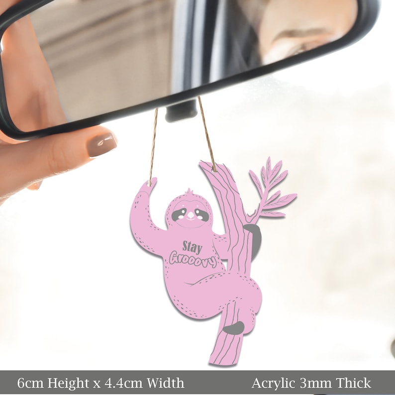 May include: Pink acrylic car air freshener shaped like a sloth hanging from a tree branch. The sloth has a happy expression and says "Stay Groovy". The air freshener is 6 inches tall and 4.4 inches wide.