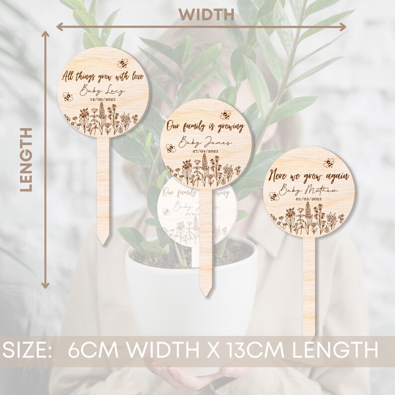 K&ouml;nnte beinhalten: Drei h&ouml;lzerne Pflanzenmarkierungen mit floralem Design und Bienen-Akzenten. Die Markierungen sind 6 cm breit und 13 cm lang. Der Text auf den Markierungen lautet: "All things grow with love Baby Ley 18/06/2005", "Our family is growing Baby James 27/04/2005" und "Neve we grow again Baby Mathew 01/05/2005".