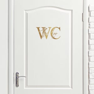 May include: A white door with a gold decal that says "WC the Loo" on it.