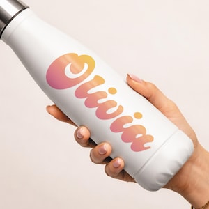 May include: White insulated water bottle with a silver cap. The bottle features the name "Olivia" in a gradient of orange and pink. The bottle is held by a person.