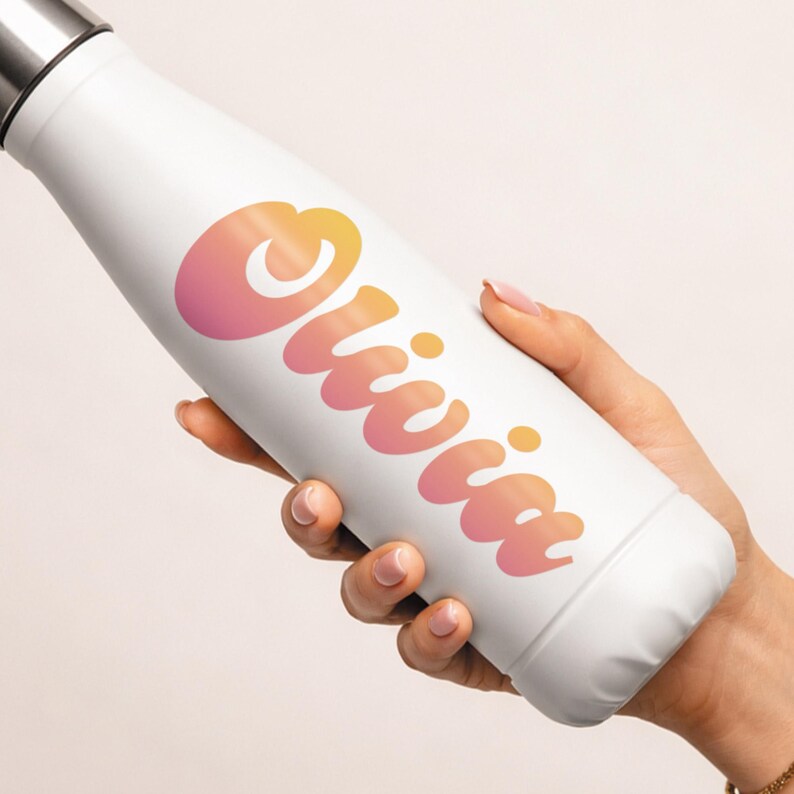 May include: White insulated water bottle with a silver cap. The bottle features the name "Olivia" in a gradient of orange and pink. The bottle is held by a person.