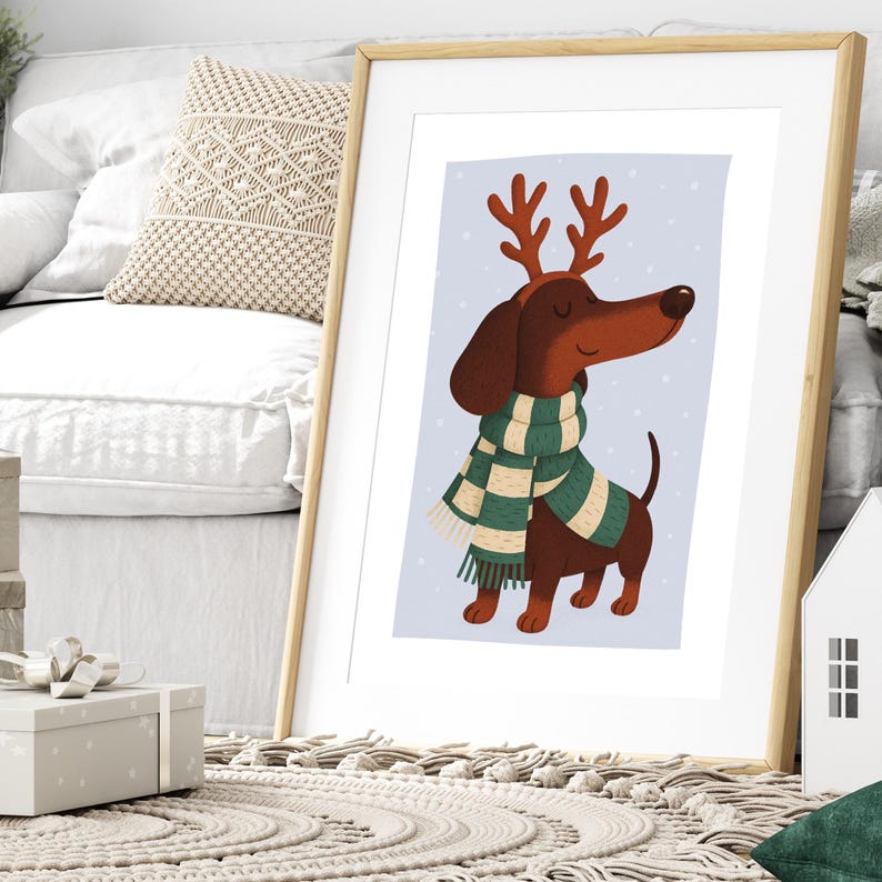 May include: A framed print featuring a cartoon dachshund wearing a green and white scarf and reindeer antlers. The dog is brown with a long snout and is set against a light blue background with white dots. The print is in a wooden frame.