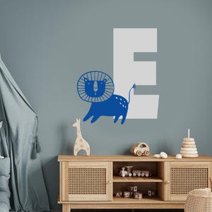 May include: Blue lion with a mane and a white letter E on a blue wall. The lion is facing right and has a tail. The letter E is behind the lion. There is a wooden shelf with toys on it.
