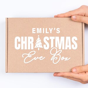 May include: A brown cardboard box with the text "Emily's Christmas Eve Box" in white lettering. The box has a small white Christmas tree graphic with a star on top.