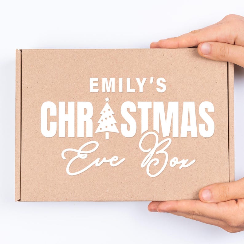 May include: A brown cardboard box with the text "Emily's Christmas Eve Box" in white lettering. The box has a small white Christmas tree graphic with a star on top.