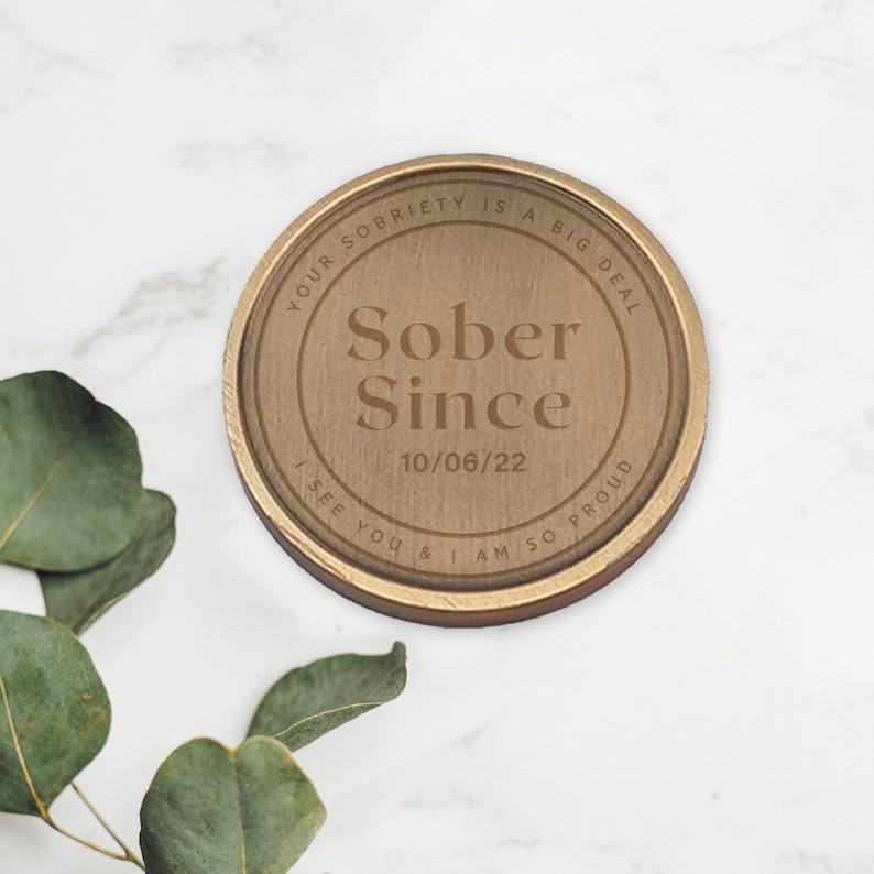 May include: A round, gold-colored metal token with the text "YOUR SOBRIETY IS A BIG DEAL" and "Sober Since 10/06/22" engraved on it. The text "I SEE YOU & I AM SO PROUD" is also engraved on the token.
