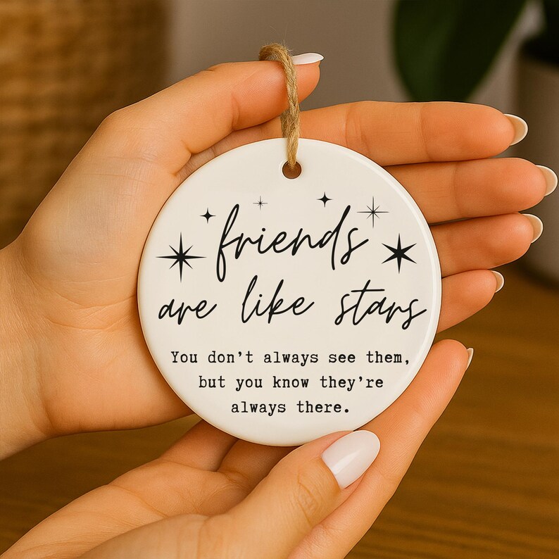 May include: A round, white ceramic ornament with the text "friends are like stars" in black script. The ornament has a jute twine loop for hanging and includes the quote, "You don't always see them, but you know they're always there."