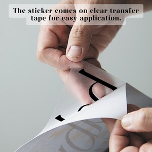 May include: A hand is peeling back a clear transfer tape from a black vinyl sticker. The sticker comes on clear transfer tape for easy application.