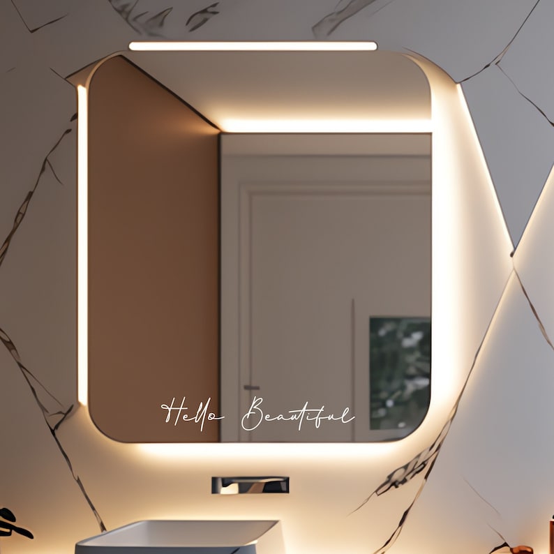 Puede incluir: Un espejo de ba&ntilde;o moderno con un borde de luz LED blanco y el texto "Hello Beautiful" escrito en la superficie del espejo.
