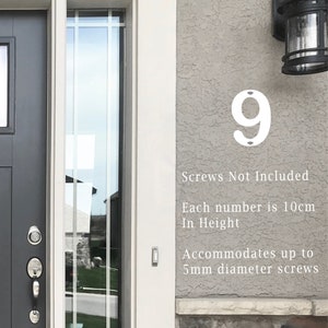 May include: White metal house number 9 fixed to a textured grey wall. The number is 10cm in height and suitable for screws up to 5mm diameter. Text on the wall reads: "Screws Not Included."