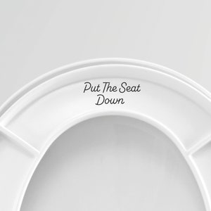 May include: White toilet seat with the text "Put The Seat Down" printed on the top.