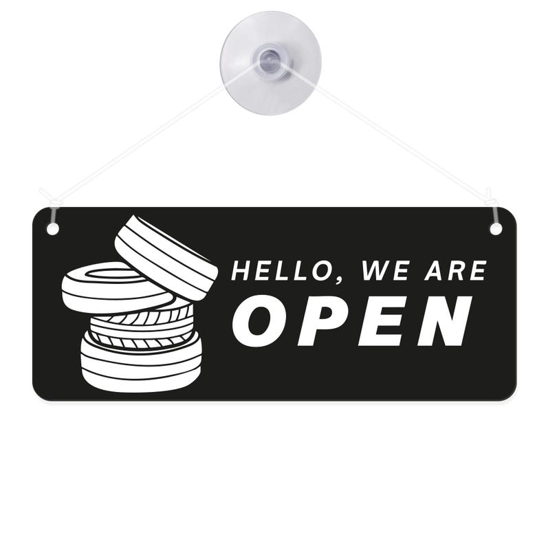 May include: Black rectangular sign with the words "HELLO, WE ARE OPEN" in white. A stack of tires is on the left side of the sign. The sign is suspended by a clear suction cup and string.
