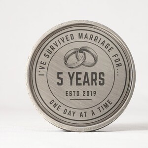 Puede incluir: Un recuerdo redondo de metal plateado con el texto "I've Survived Marriage For... 5 Years Estd 2019 One Day at a Time." Dos anillos entrelazados est&aacute;n en el centro. Los bordes tienen una apariencia texturizada.