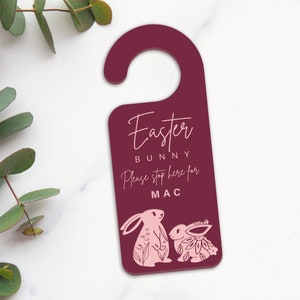 May include: A burgundy door hanger with a white inscription that reads "Easter Bunny Please stop here for MAC" and two pink bunny illustrations.