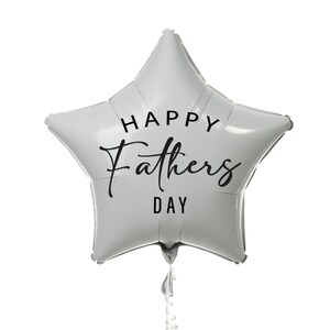 Puede incluir: Un globo plateado en forma de estrella con el texto "HAPPY Fathers DAY" en escritura negra. El globo est&aacute; inflado y tiene una cinta adjunta en la parte inferior. El globo es una decoraci&oacute;n festiva para el D&iacute;a del Padre.