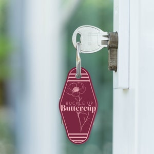May include: A maroon motel key tag with a white outline of a flower and the text "Buckle Up Buttercup".