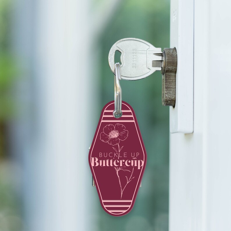 May include: A maroon motel key tag with a white outline of a flower and the text "Buckle Up Buttercup".