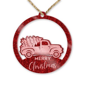 May include: Red glitter Christmas ornament with a pink silhouette of a truck carrying a Christmas tree and the text "Merry Christmas".