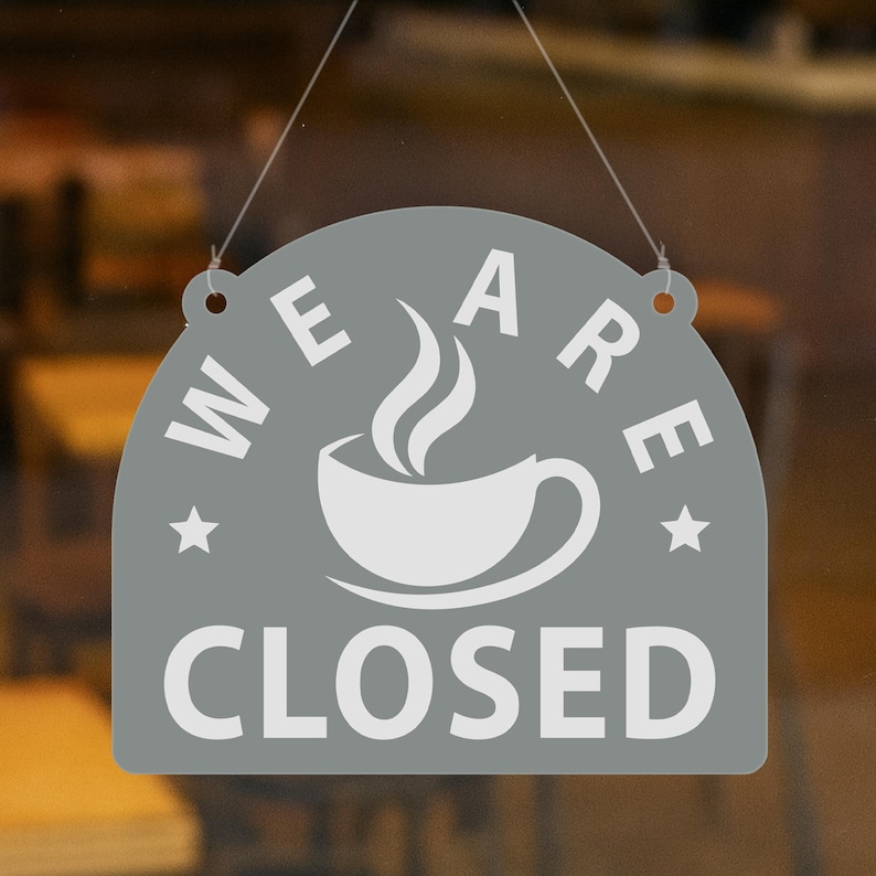 May include: A gray, semi-circular sign with the words "WE ARE CLOSED" in white lettering. A white coffee cup with steam is in the center. The sign is hanging by a thin string.