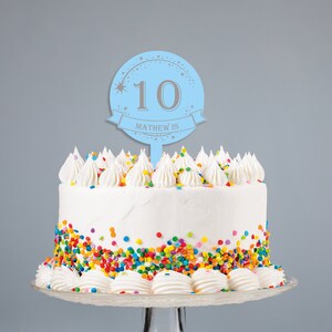 May include: Blue and silver cake topper with the number 10 and the text "Matthew is" on a white cake with colorful sprinkles.