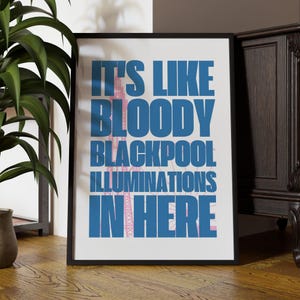 Pu&ograve; includere: Una stampa artistica incorniciata con il testo "IT'S LIKE BLOODY BLACKPOOL ILLUMINATIONS IN HERE" in blu, con un'illustrazione rosa della Blackpool Tower. La stampa &egrave; in una cornice nera, su sfondo bianco.